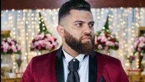 O programador Micheal Jonathan está no centro da foto. Ele usa um terno vermelho, possui barba e está olhando para o lado direito